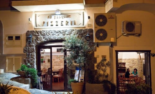 Ingresso della Pizzeria La Pesquera a Serrara Fontana con arcata in pietra coperta d'edera e posti a sedere all'aperto