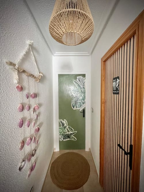 Pasillo moderno en Haus Holiday Homes con lámpara colgante tejida, arte de concha marina en pared y puerta de baño decorada con plantas verdes