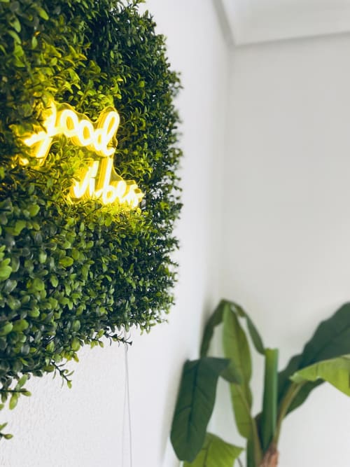 Letrero de neón amarillo en pared verde viva con plantas del apartamento Haus Holiday Homes en Lo Pagán, España