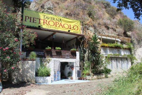 Ingresso della Taverna Pietropaolo a Serrara Fontana con insegna gialla, piante fiorite e vista collinare