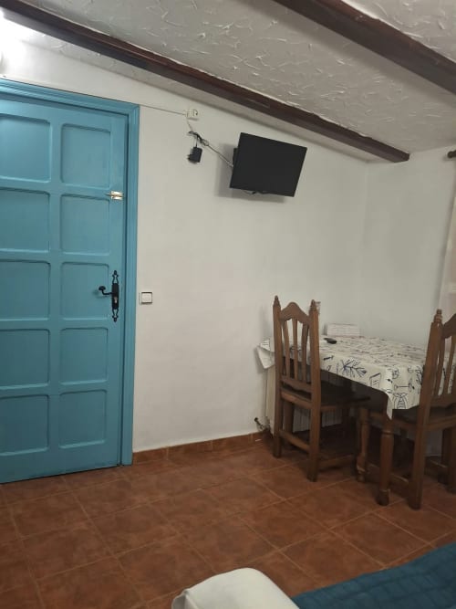 Rustic bedroom at Refugio la Presa with turquoise door, wooden chairs, flat-screen TV, terracotta floor, and exposed beam