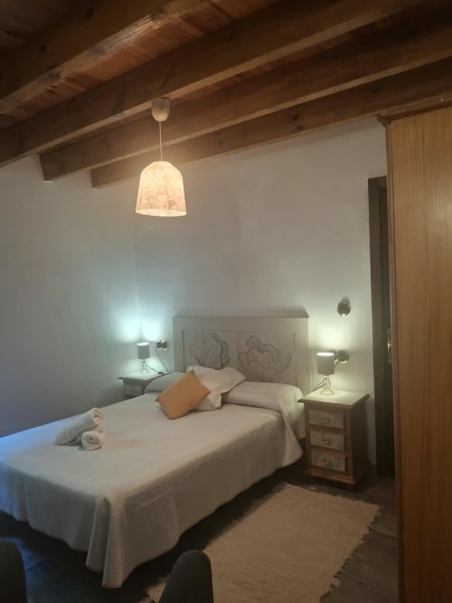 Cozy double bedroom at Refugio la Presa with white bed, wooden beams, pendant light, and bedside lamps