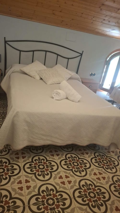 Bright bedroom at Refugio la Presa with wrought iron bed, white linens, cream patterned tiles, wooden ceiling, and bright