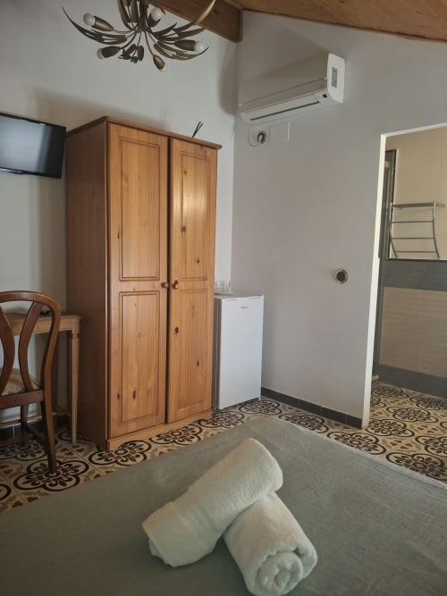 Hotel room at Refugio la Presa in Chulilla with wooden wardrobe, AC unit, bed with towels, and patterned tile floor