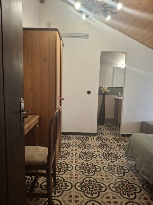 Bedroom at Refugio la Presa hotel in Chulilla with decorative tile flooring, wooden wardrobe, bed, and ensuite bathroom