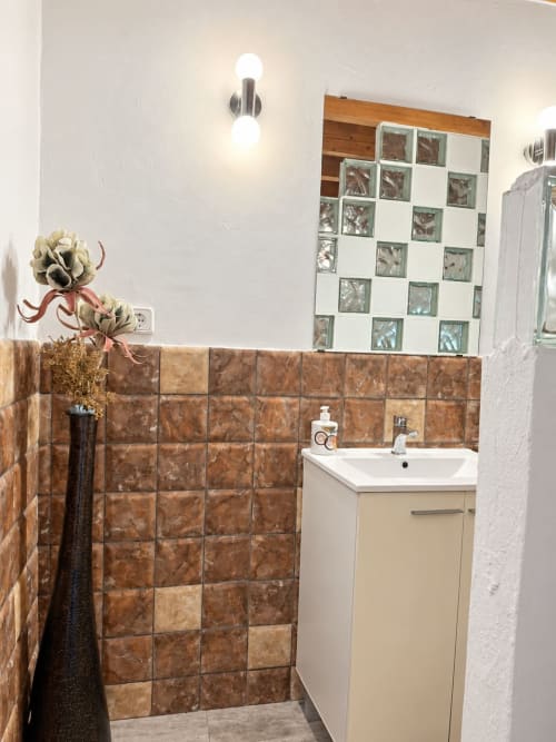 Modern bathroom at Refugio la Presa in Chulilla with brown tile accents, white vanity, and decorative mirror.