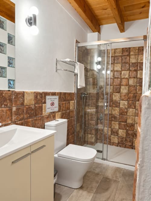 Modern bathroom at Refugio la Presa in Chulilla with brown tile shower, white vanity, and heated towel rack