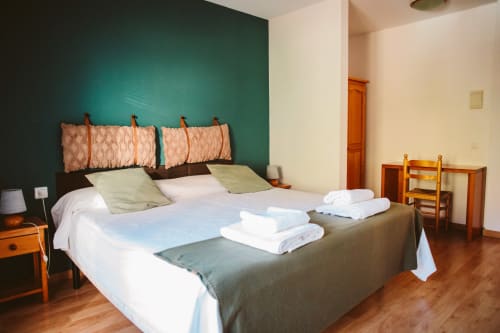 Spacious double bedroom at Balcó del Priorat hotel in Tarragona with turquoise accent wall, wooden furnishings, and fresh