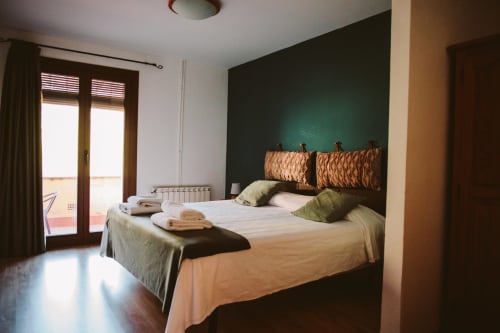 Amplía habitación en Balcó del Priorat con pared de acentó verde oscuro, cama doble, cabecero tejido, puertas al balcón y montañas