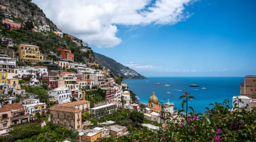 Pittoresco villaggio di Positano arroccato sulla scogliera con chiesa dalla cupola dorata che affaccia sul turchese Mar Mediterraneo, Italia