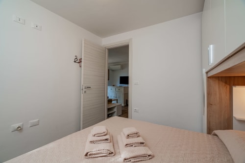 Camera da letto con letto, asciugamani piegati e porta aperta verso il cucinotto dell'appartamento Short Let's Olbia a Olbia, Italia
