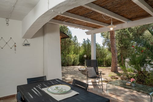 Patio coperto con tavolo da pranzo, lettino relax e vista sul giardino boscoso a Olbia