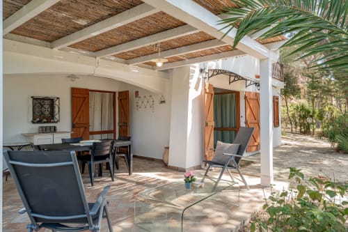 Ampio patio di Short Let's Olbia con sdraio, tavolo da pranzo, travi bianche e rigogliosa vegetazione