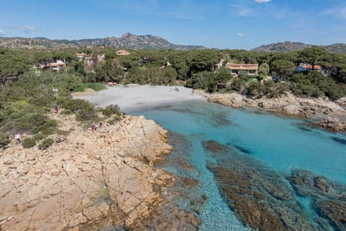 Caletta turchese con spiaggia sabbiosa, costa rocciosa e ville mediterranee tra le colline verdi vicino a Olbia