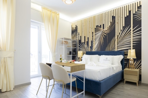 Lussuosa camera da letto alle Aurum Nolana Suites di Pompei con letto blu navy, carta da parati con foglie di palma e vista balcone sulla città