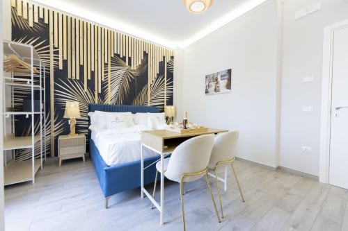 Camera deluxe presso Aurum Nolana Suites di Pompeii con letto blu, carta da parati con palme dorate e scrivania