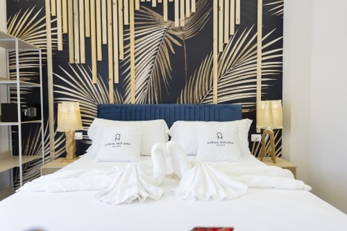 Lussuoso letto matrimoniale con asciugamani arrotolati presso Aurum Nolana Suites a Pompei, con testiera blu navy e carta da parati con foglie di palma dorate