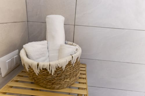 Cesto intrecciato con asciugamani bianchi e rotolo di carta igienica su ripiano in legno nel bagno di Aurum Nolana Suites, Pompei