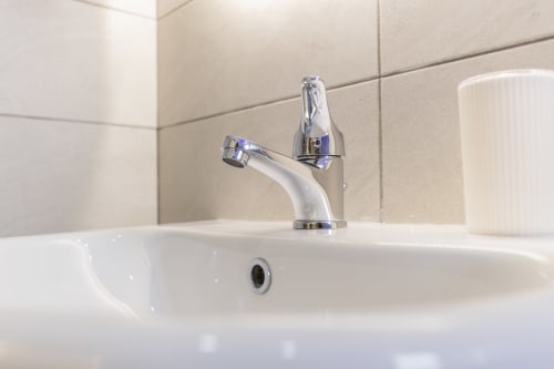 Moderno lavabo bianco con rubinetto cromato nella suite Aurum Nolana, bagno con piastrelle beige