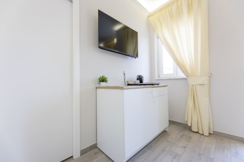 Moderna cucina con mobili bianchi, TV a schermo piatto e finestra con vista città e tende color crema presso Aurum Nolana Suites,