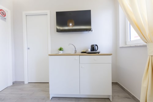 Piccolo angolo cottura con mobili bianchi, piano in legno, lavello e TV nella suite Aurum Nolana Suites Pompei
