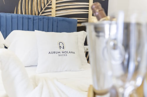 Camera Aurum Nolana Suites con testata blu, cuscino brandizzato bianco, elegante biancheria da letto e vista sulla città di Pompei