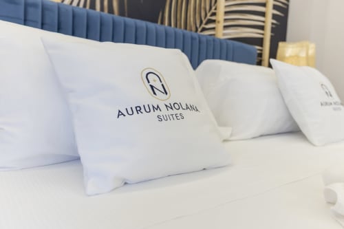 Cuscini brandizzati Aurum Nolana Suites su letto deluxe con testata blu, camera hotel Pompeii