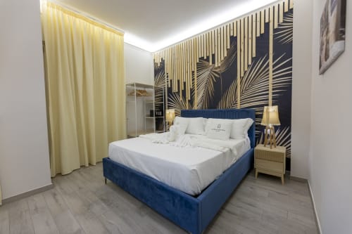 Camera da letto doppia deluxe presso l'Aurum Nolana Suites a Pompei con letto blu navy, dettagli oro e testiera con motivi botanici scuri