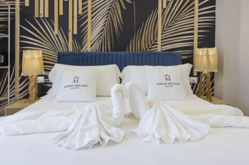 Camera deluxe delle Aurum Nolana Suites Pompei con letti matrimoniali, biancheria bianca, testata blu navy e carta da parati con foglie di palma dorate