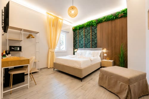 Camera tripla moderna presso Aurum Nolana Suites a Pompeii con vista montagna, letto beige, parete verde con piante, scrivania e atmosfera calda