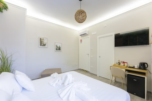 Camera moderna presso Aurum Nolana Suites a Pompei con letto bianco, lampada sospesa in vimini, scrivania in legno e vista sulle montagne