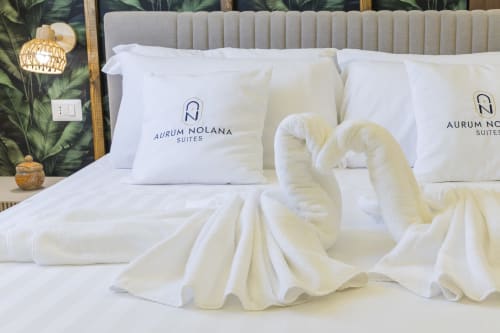 Lussuoso letto presso l'Aurum Nolana Suites a Pompei con cuscini branded, biancheria bianca e asciugamani piegati con vista montuosa.