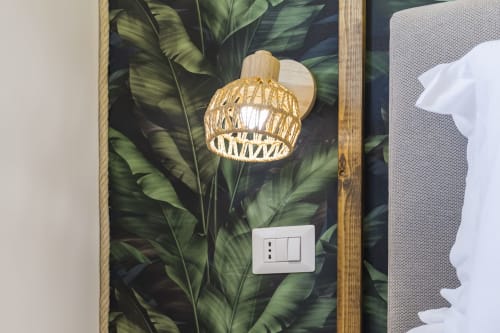 Lampada sospesa in rattan intrecciato davanti a carta da parati tropicale, interruttore della luce sottostante, dettaglio camera Aurum Nolana Suites