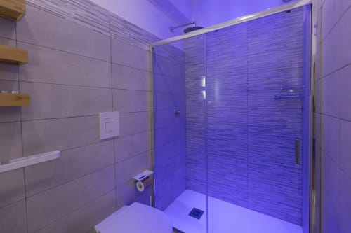 Bagno moderno con illuminazione viola, box doccia in vetro e rivestimenti in marmo presso l'Aurum Nolana Suites di Pompei