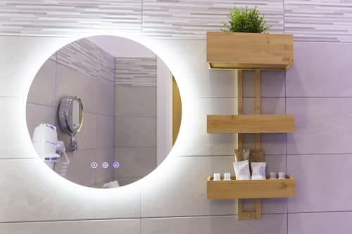 Bagno moderno presso Aurum Nolana Suites con specchio circolare illuminato, mensole in legno con articoli da toilette e lavanda