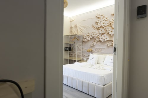 Camera da letto lussuosa presso Aurum Nolana Suites a Pompeii con letto king, biancheria bianca, decorazione murale floreale bianca e