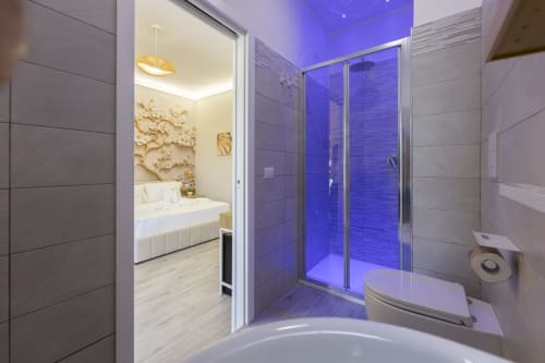 Bagno moderno con doccia illuminata di blu, wc bianco e vista sulla camera presso Aurum Nolana Suites a Pompei