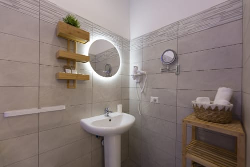 Bagno moderno con specchio illuminato, lavabo su colonna, mensole in legno e piastrelle beige presso Aurum Nolana Suites a Pompei