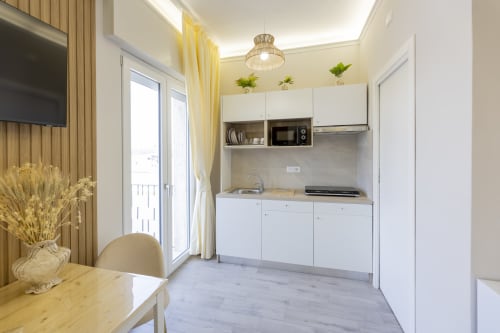 Cucina moderna nella suite Aurum Nolana Suites Pompeii con mobili bianchi, zona pranzo, tende gialle e accesso al balcone