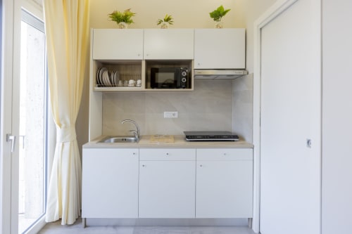 Cucina moderna in Aurum Nolana Suites, Pompei: armadi bianchi, fornello, lavello, microonde e mensole aperte con piante