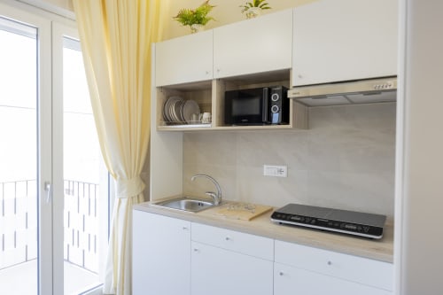 Angolo cottura moderno con mobili bianchi, microonde e piano cottura nella Executive Triple Room di Aurum Nolana Suites, Pompei
