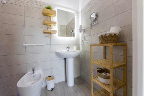 Moderno bagno delle Aurum Nolana Suites di Pompei con lavabo su colonna, bidet, scaffalature in legno e pareti piastrellate