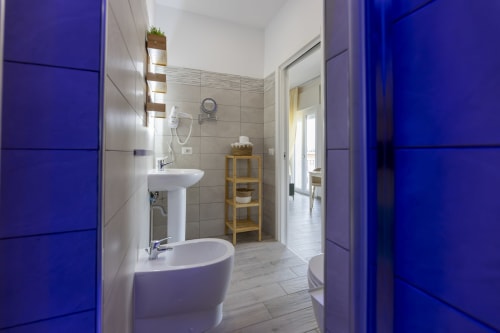 Bagno moderno presso l'Aurum Nolana Suites di Pompei con mobili blu, lavabo su colonna, bidet e mensole in legno