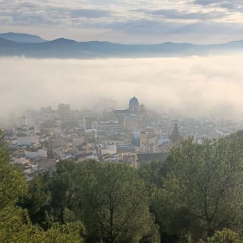 Misty morning aerial view of Yecla cityscape with cathedral dome, mountains, and forested hills in Spain
