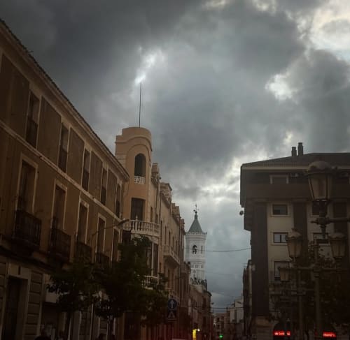 Historic Yecla street with traditional architecture and church tower under dramatic cloudy sky