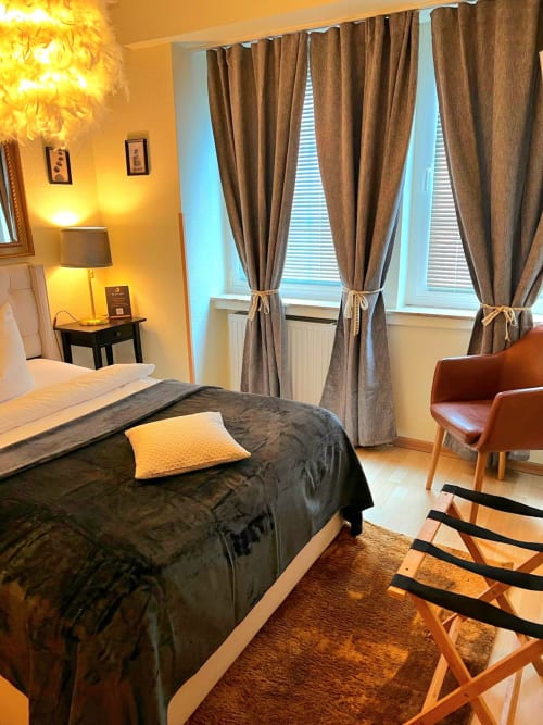 Modernes Hotelzimmer des Soho Hotel Düsseldorf mit Doppelbett, warmer Beleuchtung, braunen Vorhängen und zeitgenössischen Möbeln