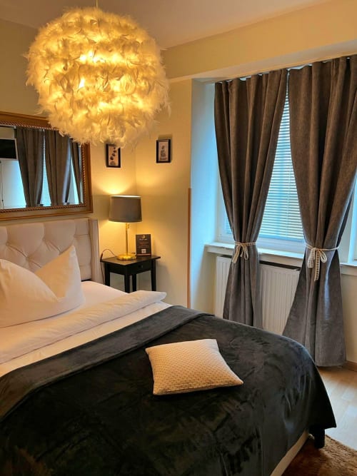 Elegantes Schlafzimmer im The Soho Hotel Düsseldorf mit Federpendel, cremefarbenes Kopfteil und braune Vorhänge.