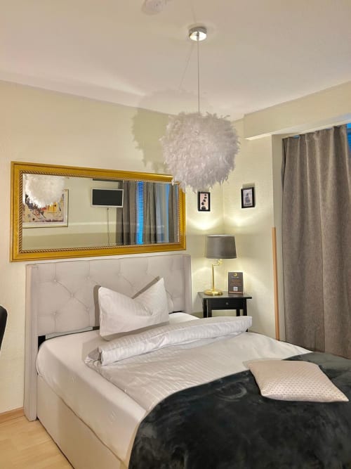 Soho Hotel Düsseldorf Schlafzimmer mit weißem Polsterbett, goldenem Spiegel, Federpendel und cremefarbenen Wänden