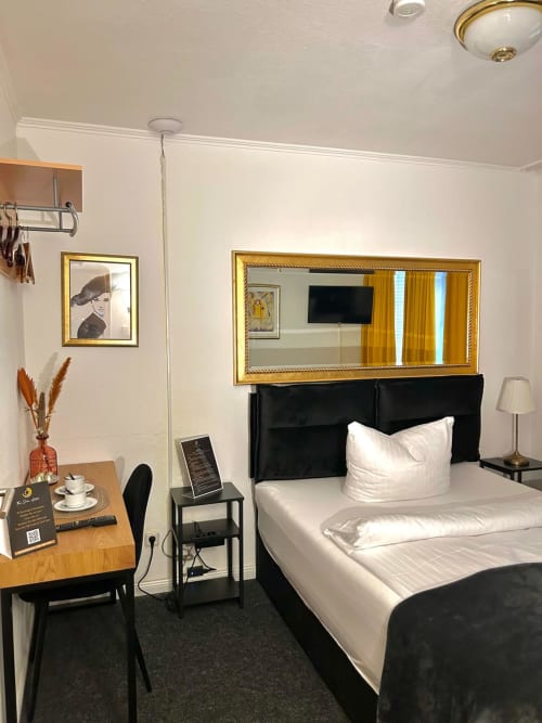 Modernes Hotelzimmer im The Soho Hotel Düsseldorf mit schwarzem Bett, goldenem Spiegel, Holzschreibtisch und zeitgenössischer Einrichtung