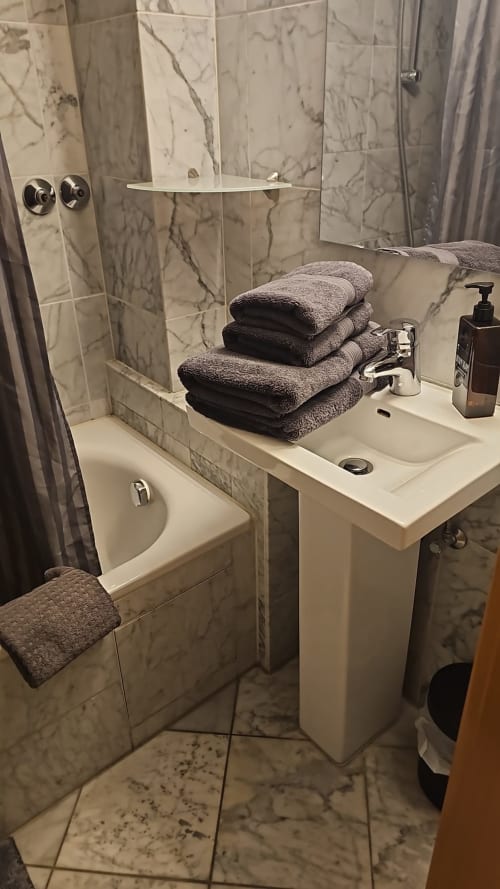 Modernes Badezimmer im Soho Hotel Düsseldorf mit Marmorfliesen, Säulenwaschbecken und gefalteten grauen Handtüchern